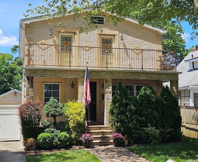 view of front of house with brick siding, a balcony, and fence