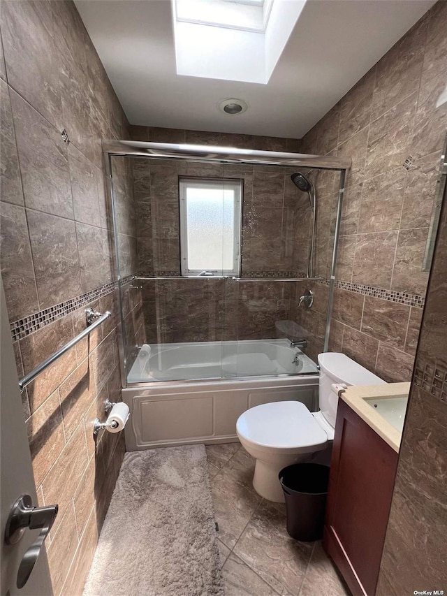 full bathroom with toilet, tile walls, a skylight, enclosed tub / shower combo, and vanity