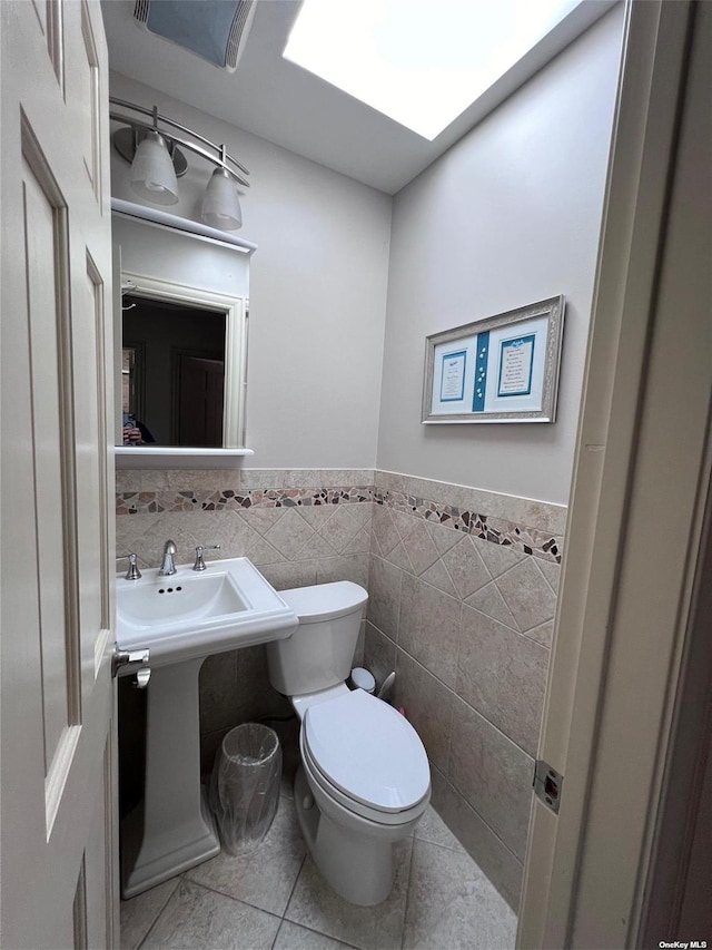 bathroom with tile patterned floors, toilet, tile walls, a skylight, and wainscoting