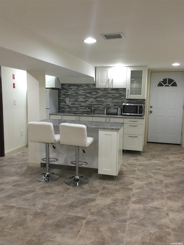 kitchen featuring stainless steel microwave, tasteful backsplash, visible vents, and freestanding refrigerator