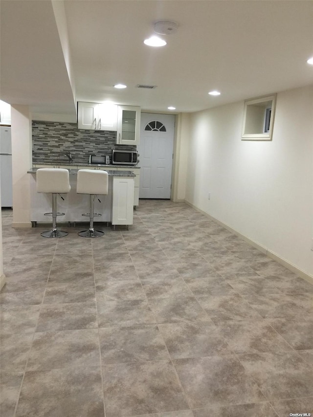 kitchen with stainless steel microwave, tasteful backsplash, white cabinetry, freestanding refrigerator, and a breakfast bar area