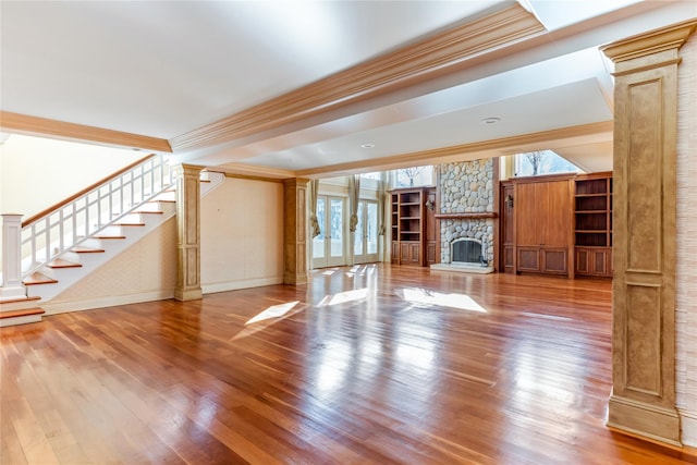 unfurnished living room with stairs, crown molding, ornate columns, and wood finished floors