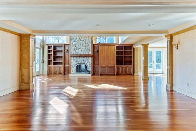 unfurnished living room featuring crown molding, baseboards, a fireplace, wood finished floors, and ornate columns