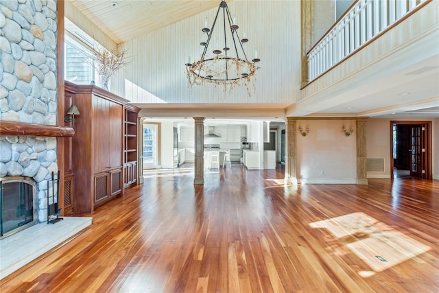 unfurnished living room with baseboards, hardwood / wood-style floors, a stone fireplace, an inviting chandelier, and ornate columns