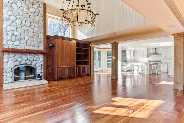 unfurnished living room featuring light wood finished floors, a stone fireplace, a high ceiling, and ornate columns