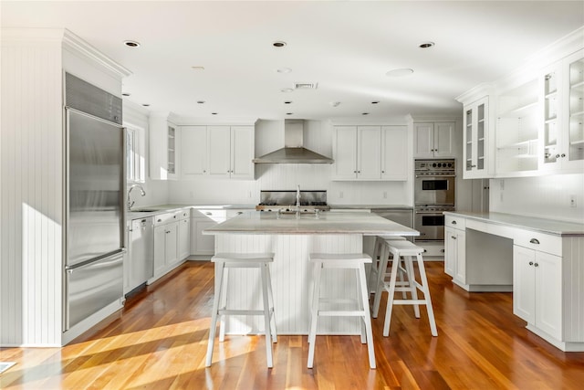 kitchen with a kitchen island with sink, a sink, appliances with stainless steel finishes, wall chimney exhaust hood, and light countertops