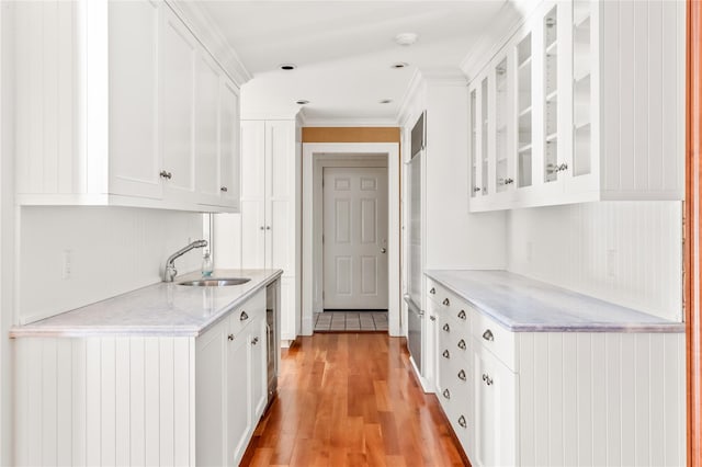 kitchen featuring light wood-type flooring, a sink, white cabinetry, crown molding, and glass insert cabinets