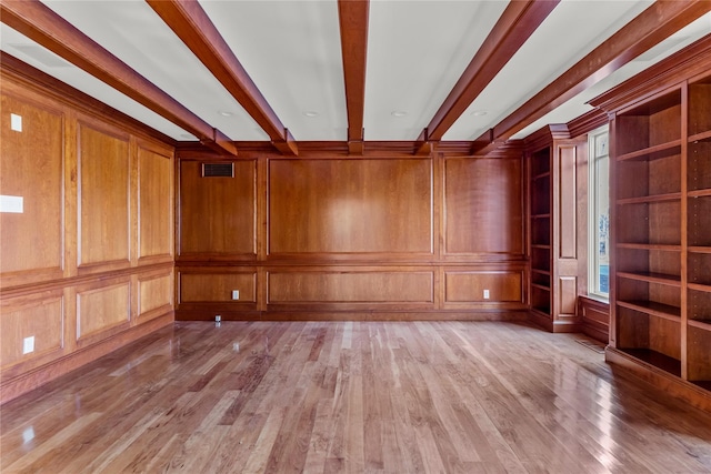 spare room with visible vents, beam ceiling, light wood-style flooring, and a decorative wall