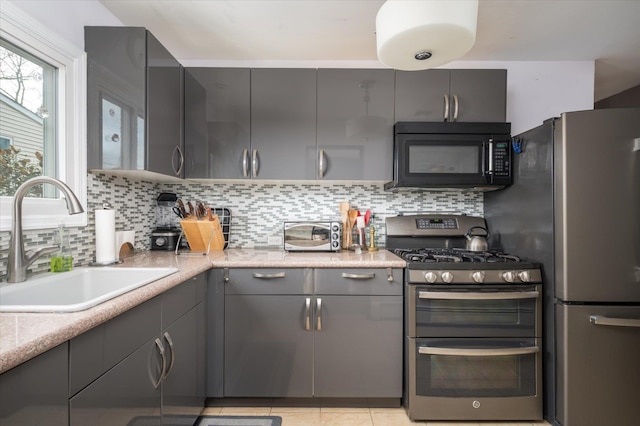 kitchen featuring decorative backsplash, gray cabinets, stainless steel appliances, and a sink