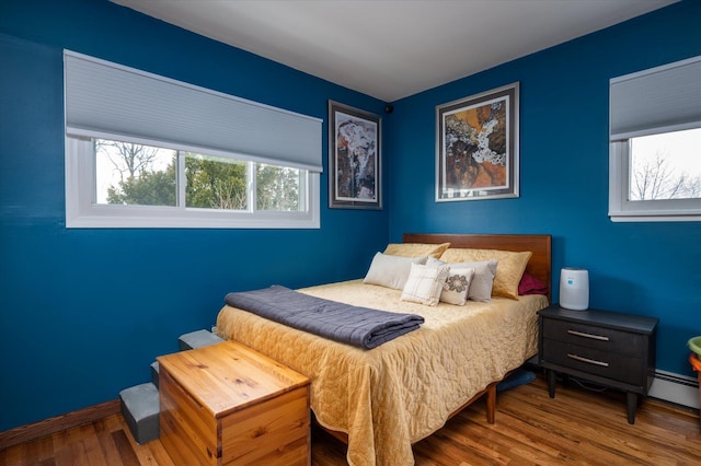 bedroom featuring a baseboard heating unit, baseboards, and wood finished floors