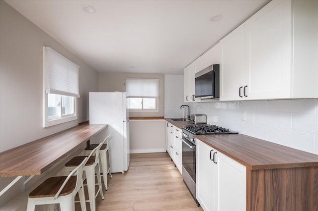 kitchen with backsplash, butcher block countertops, appliances with stainless steel finishes, white cabinetry, and a sink