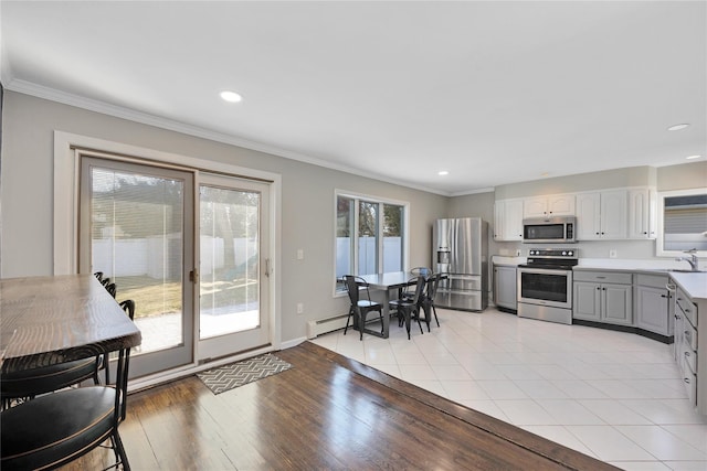 kitchen featuring light wood-type flooring, ornamental molding, gray cabinets, stainless steel appliances, and light countertops