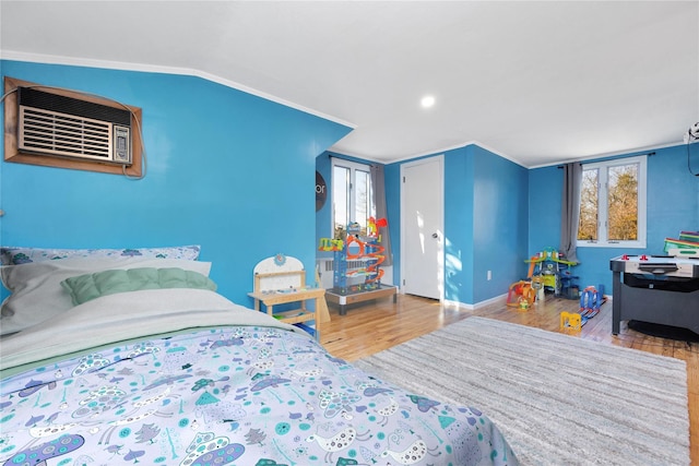 bedroom featuring wood finished floors, baseboards, lofted ceiling, a wall mounted air conditioner, and crown molding