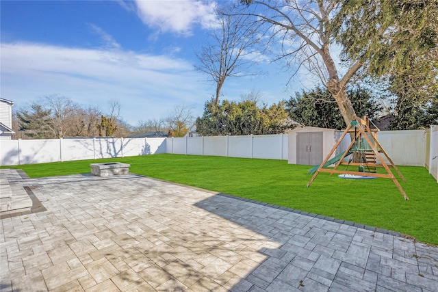 view of patio with an outbuilding, a shed, a fenced backyard, a fire pit, and a playground