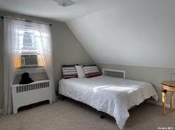 carpeted bedroom featuring cooling unit, radiator, and vaulted ceiling