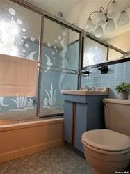 bathroom featuring tile walls, shower / bath combination with glass door, a healthy amount of sunlight, and toilet