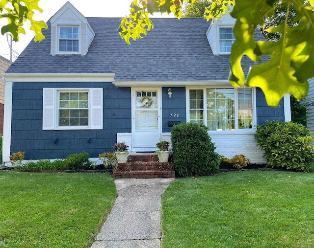 cape cod house with entry steps, a front yard, and roof with shingles