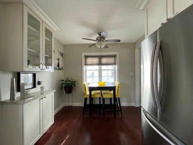 kitchen featuring dark wood finished floors, freestanding refrigerator, glass insert cabinets, baseboards, and ceiling fan