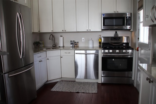 kitchen featuring light stone counters, appliances with stainless steel finishes, dark wood-style floors, white cabinetry, and a sink