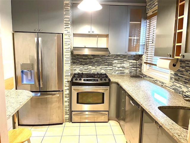 kitchen with backsplash, stainless steel appliances, wall chimney exhaust hood, light tile patterned floors, and light stone countertops