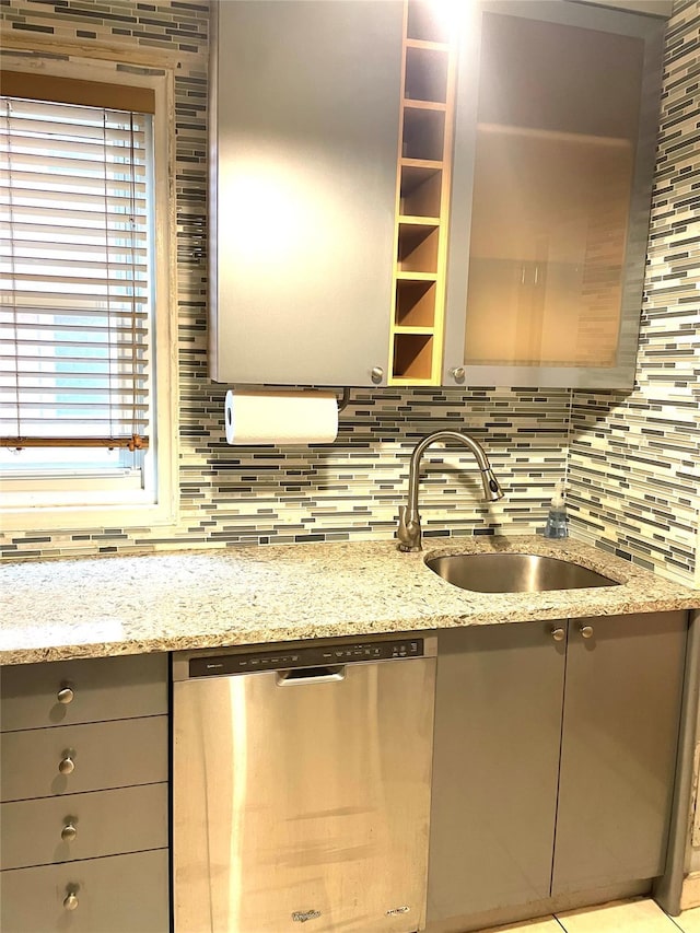 kitchen featuring backsplash, gray cabinetry, dishwasher, light stone counters, and a sink