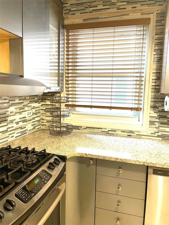 kitchen with tasteful backsplash, stainless steel range with gas stovetop, light stone counters, and exhaust hood