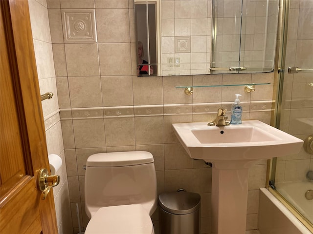 bathroom featuring toilet, a sink, shower / bath combination with glass door, tile walls, and decorative backsplash