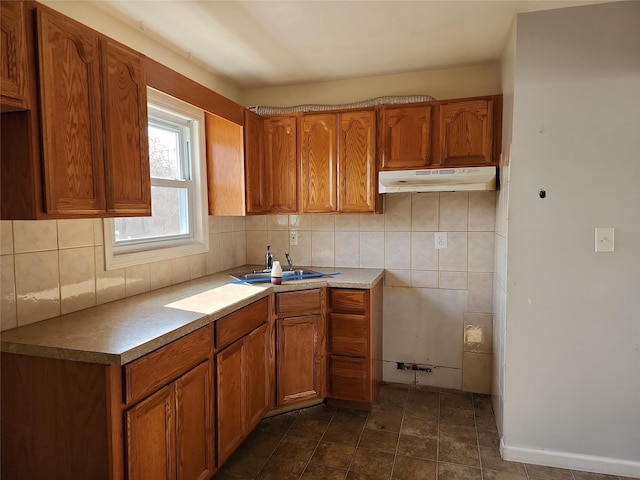 kitchen with brown cabinetry, under cabinet range hood, and a sink