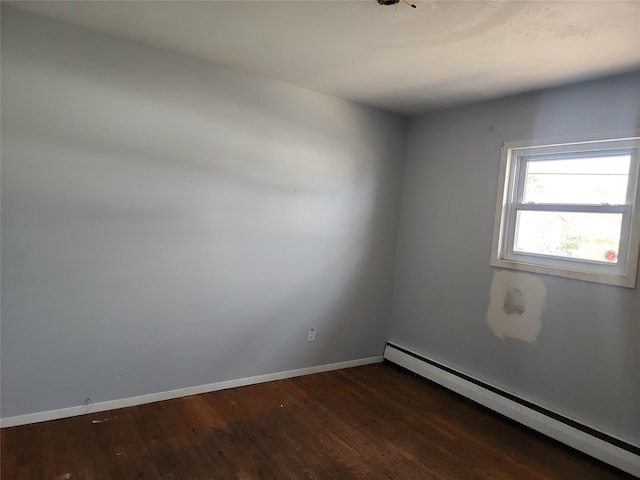 empty room featuring a baseboard heating unit, wood finished floors, and baseboards