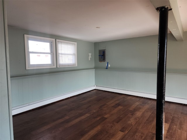 unfurnished room featuring dark wood-style flooring, baseboard heating, and wainscoting