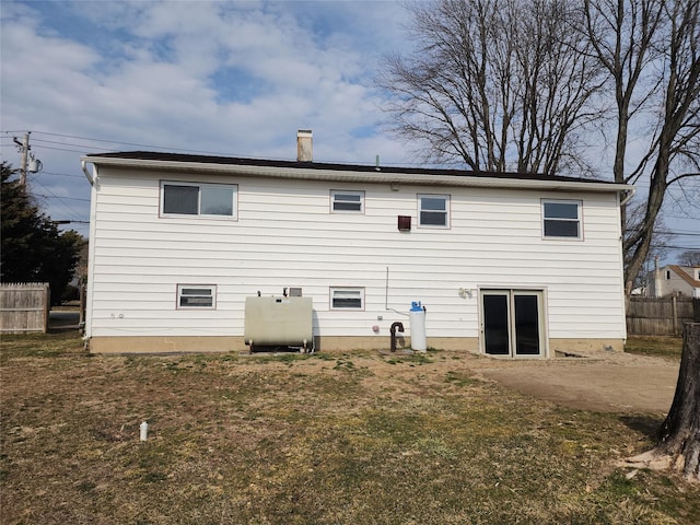 back of house featuring a patio, fence, a yard, a chimney, and heating fuel