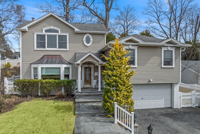 traditional-style home with a front yard, an attached garage, fence, and roof with shingles