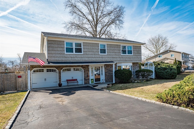 colonial home with aphalt driveway, stone siding, a front yard, and fence