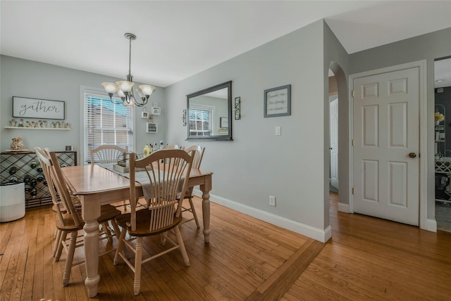 dining space featuring an inviting chandelier, baseboards, arched walkways, and light wood-type flooring