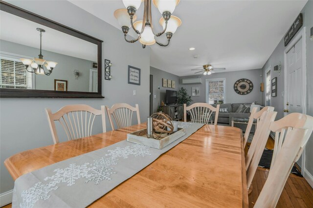 dining room with ceiling fan with notable chandelier, a wall mounted AC, and wood finished floors