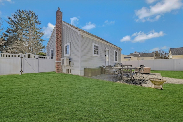 rear view of property featuring a patio, a gate, a fenced backyard, a chimney, and a lawn