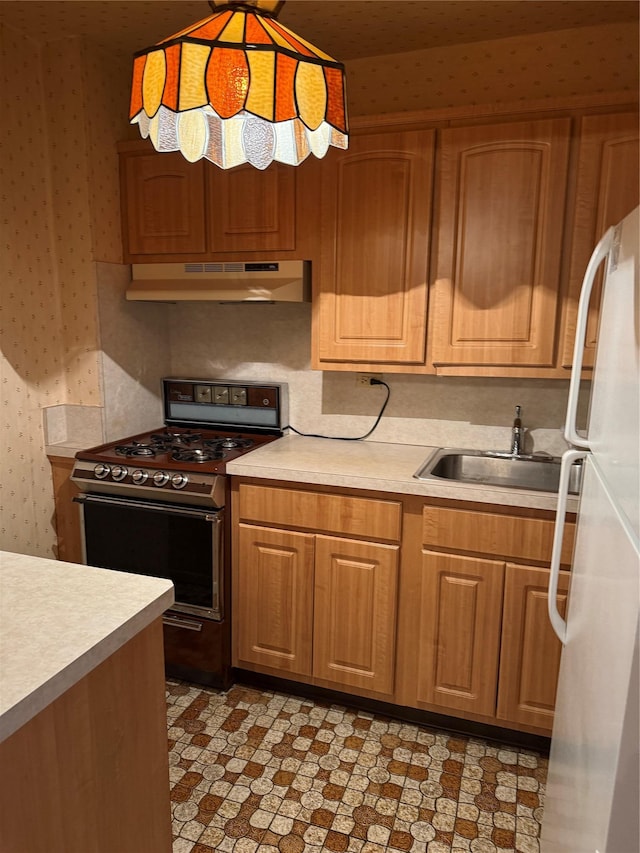 kitchen featuring under cabinet range hood, wallpapered walls, freestanding refrigerator, and gas range oven