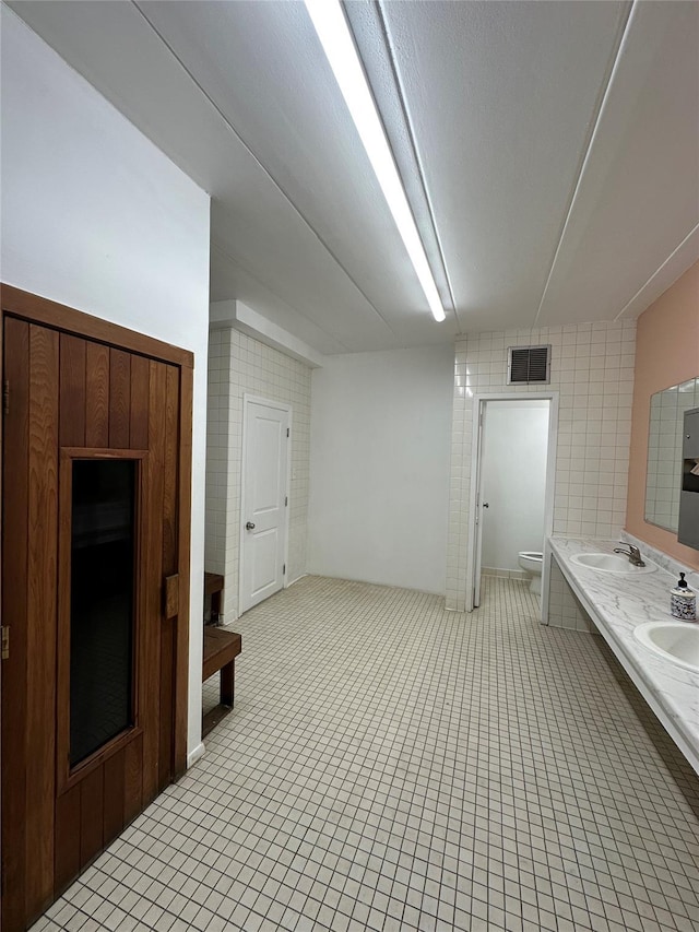 bathroom featuring visible vents, double vanity, a sink, tile patterned flooring, and toilet