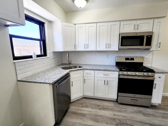 kitchen with a sink, light stone counters, appliances with stainless steel finishes, and white cabinetry