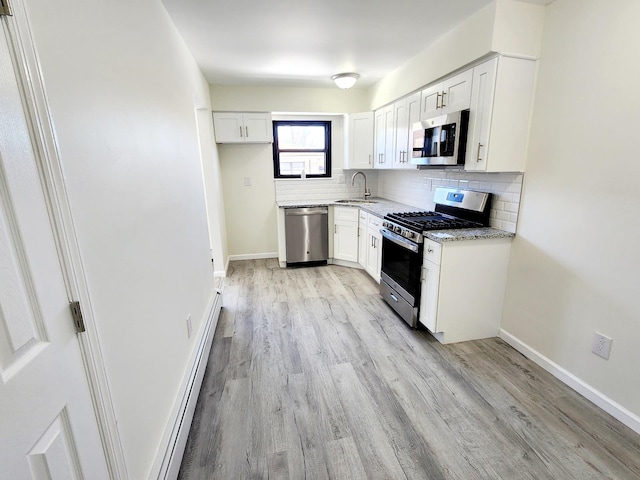 kitchen featuring a sink, a baseboard heating unit, appliances with stainless steel finishes, decorative backsplash, and light stone countertops