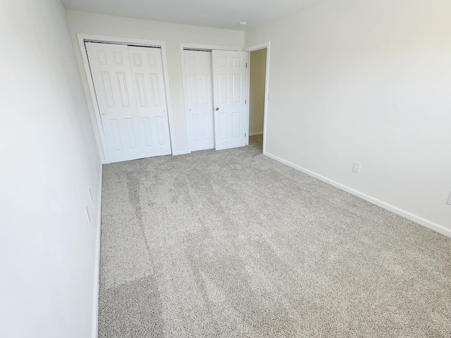 unfurnished bedroom with carpet, baseboards, and two closets