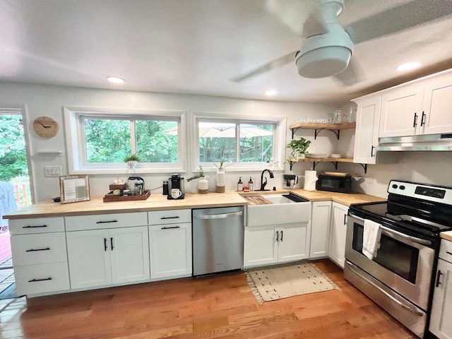 kitchen with open shelves, a sink, light wood-type flooring, appliances with stainless steel finishes, and under cabinet range hood