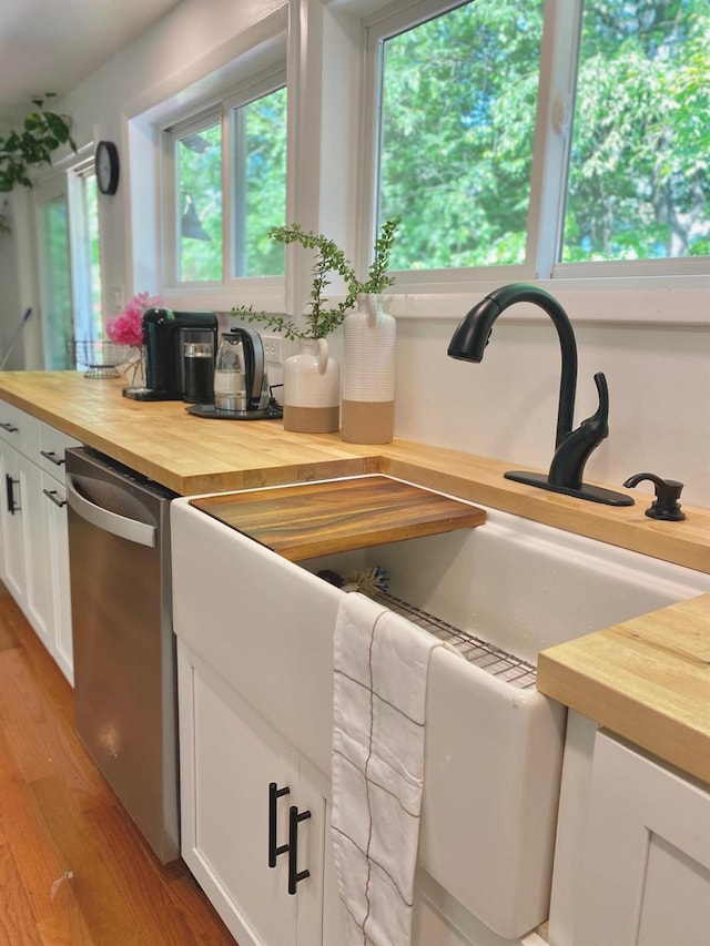 kitchen featuring light wood-style floors, a healthy amount of sunlight, white cabinetry, butcher block countertops, and stainless steel dishwasher