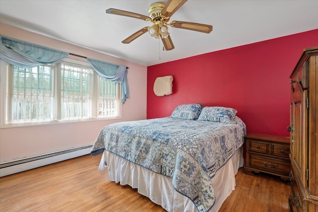 bedroom with baseboard heating, an accent wall, ceiling fan, and wood finished floors