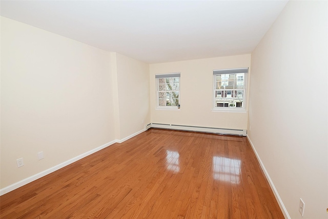 unfurnished room featuring a baseboard heating unit, baseboards, and wood finished floors