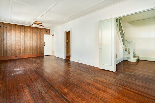 unfurnished room featuring wooden walls, baseboards, ceiling fan, stairway, and hardwood / wood-style floors