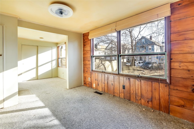 spare room featuring visible vents, carpet flooring, and wood walls