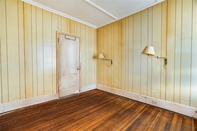 empty room featuring baseboards, dark wood-style flooring, wood walls, and ornamental molding