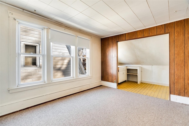 carpeted spare room with baseboards, baseboard heating, and wooden walls