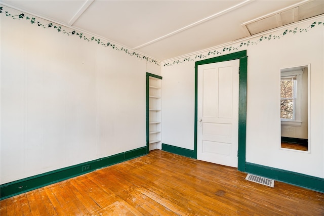 unfurnished room featuring visible vents, baseboards, attic access, and hardwood / wood-style floors